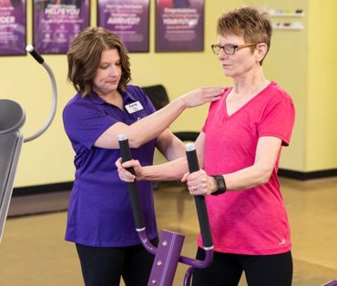 Curves coach assisting woman using an exercise machine