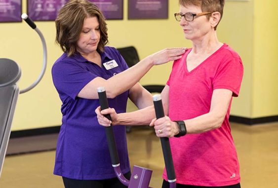Curves coach assisting woman using an exercise machine