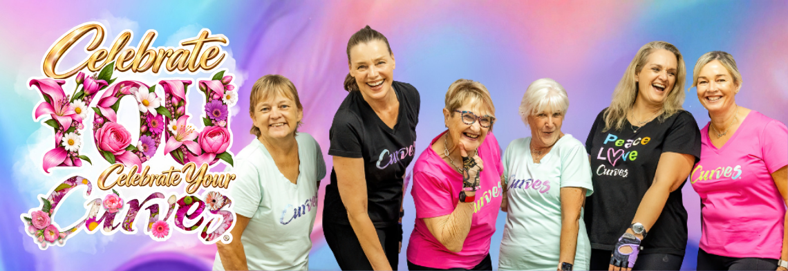 Promotional horizontal banner for Curves featuring a group of six smiling women of diverse ages standing side-by-side against a soft blue and purple gradient background. They are wearing varied Curves workout t-shirts in black, mint green, and bright pink. On the left side of the banner, the stylized gold and pink promotional text reads "Celebrate YOU, Celebrate Your Curves," with the words "YOU" and "Curves" intricately filled with vibrant pink roses, lilies, and green leaves.