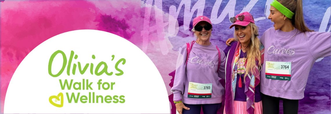 • Three smiling women wearing pink caps and purple Curves sweaters with event race bibs pose together in front of an Olivia's Walk for Wellness backdrop.